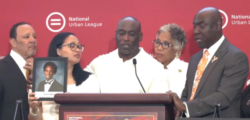Ben Crump at the podium with the families of Nolan Wells, Daniel Erving and Tyler Smith, holding a photo of Nolan Wells, at the National Urban League conference in Nashville