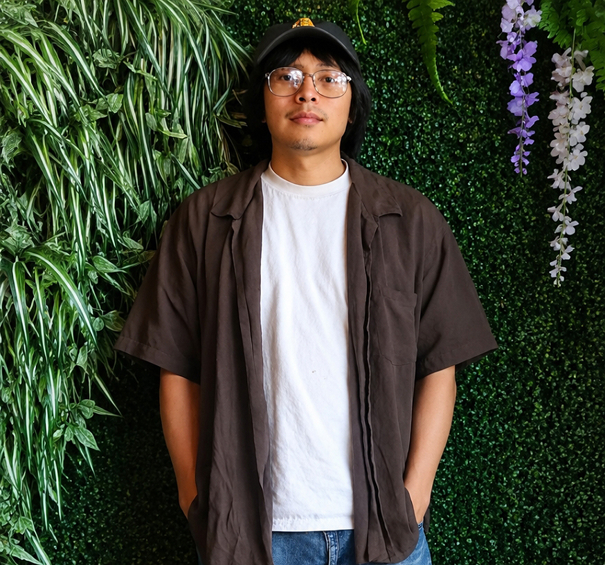 Samuel Gonzalez Terrones, 21, in a family photo: a young man in glasses, a dark cap, a white T-shirt and an open brown shirt, standing in front of a wall of plants.