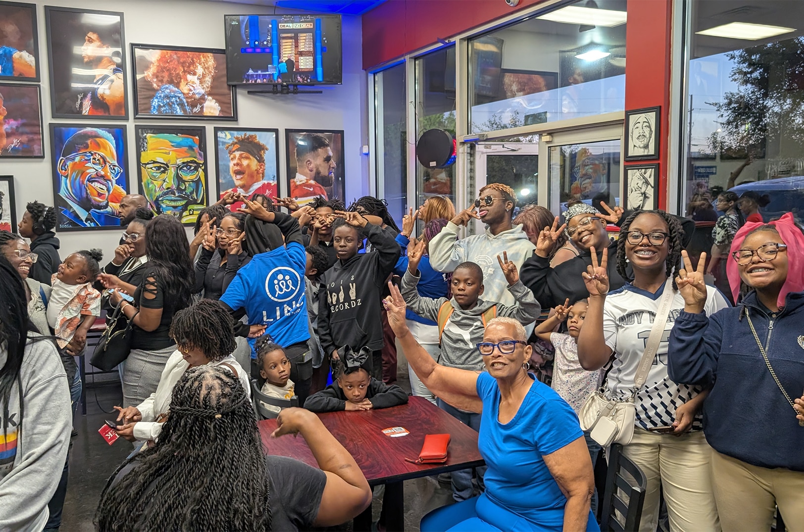 A packed restaurant full of Black mothers, children and families throwing up peace signs and smiling at The People’s Buyout during Black Feast Week 2024 in Kansas City