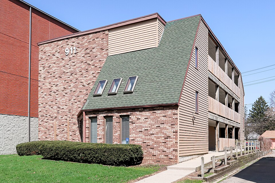 Street-level photo: In downtown East Lansing, Michigan, was 911 E Grand River Ave, on the north side of East Grand River Avenue (Michigan Highway M-43), opposite Bogue Street. The building contains commercial office space and apartments, and was built in 1988 according to its property record.